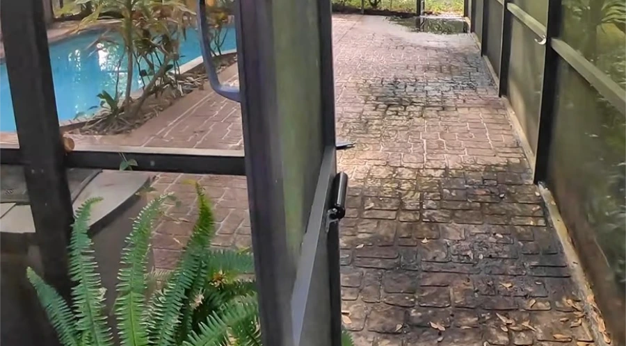 Pool deck pavers inside a screen enclosure, dark and stained before cleaning