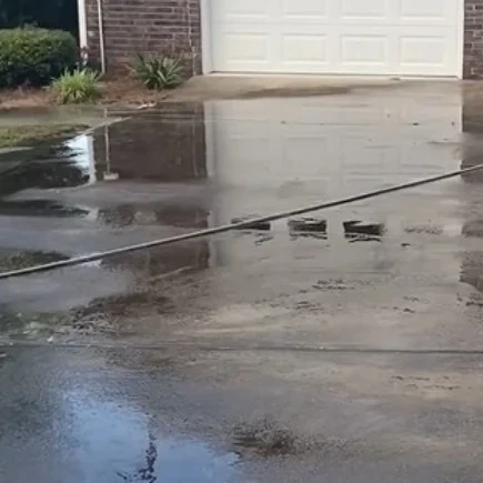 Concrete driveway at a Boynton Beach home with dirt and standing water before pressure washing